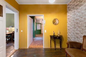 Una habitación con piso de madera, una puerta verde, un espejo y una pequeña mesa con una estatua.