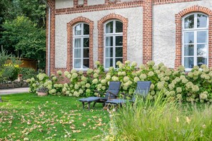 A brick building with arched windows and a garden with hydrangea bushes and two lounge chairs. - Apartment 'Gutsherren Räume Im Gutshaus Groß' with Wi-Fi (Gülzow-Prüzen)