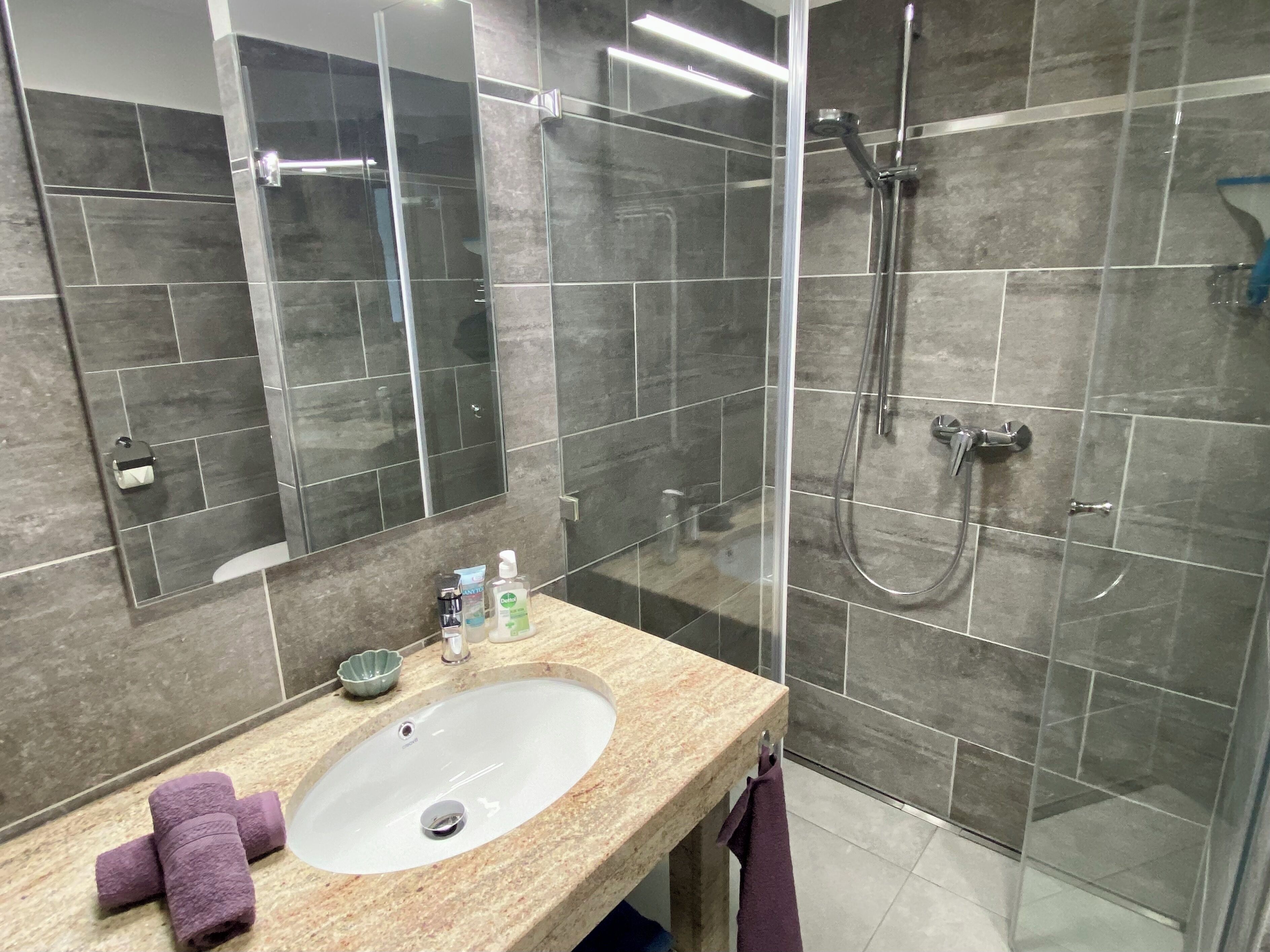 Une salle de bain moderne avec un lavabo en marbre, une cabine de douche en verre et un grand miroir.
