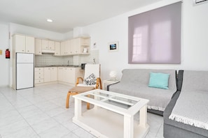 A compact living space with a kitchenette, a sofa, a coffee table, and a large window. - Apartment 'N1' with Shared Pool, Wi-Fi, and Air Conditioning (Nerja)