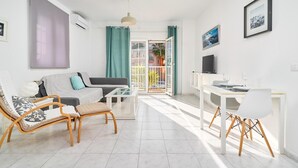 A modern living room with a sofa, a coffee table, a TV, and a dining area with chairs. - Apartment 'N1' with Shared Pool, Wi-Fi, and Air Conditioning (Nerja)