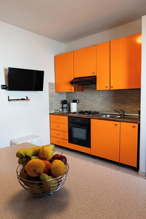 A modern kitchen with orange cabinets, a black stove, and a countertop with a coffee machine.