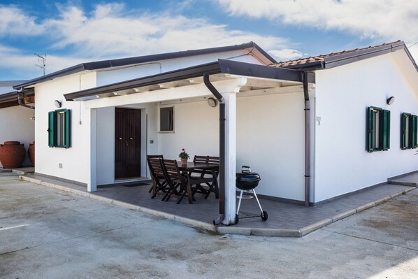 A covered patio with a table and chairs, a barbecue grill, and a door leading to a building.