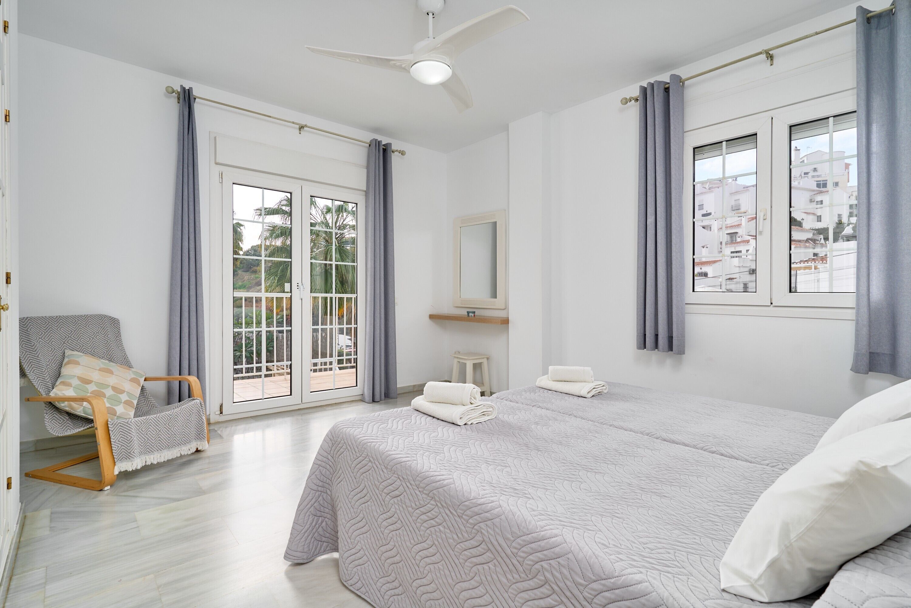 Un dormitorio con cama, una silla, un ventanal y ventilador de techo.