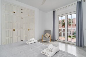 Un dormitorio con una cama grande, una silla, un armario y vistas a través de un ventanal.