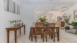 A dining area with a wooden table and chairs, a staircase, and a view into another room.