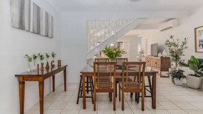 A dining area with a wooden table and chairs, a staircase, and a view into another room. - Mango Tree 2 -  relaxed coastal retreat in the heart (Byron Bay)