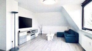 Ett modernt vardagsrum med en platt-TV, en soffa, ett soffbord och en golvlampa.