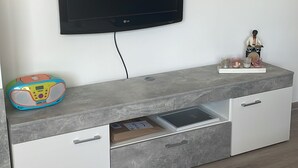Ett modernt vardagsrum med en platt-TV som är monterad på väggen, ett grått avlastningsbord med lådor och en liten dekorativ figur på bordet.