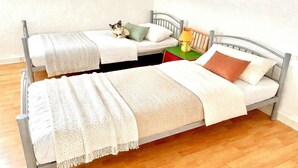 En dubbelsäng med ett vitt och beige täcke, en brun kudde och en liten hund som ligger på sängen.