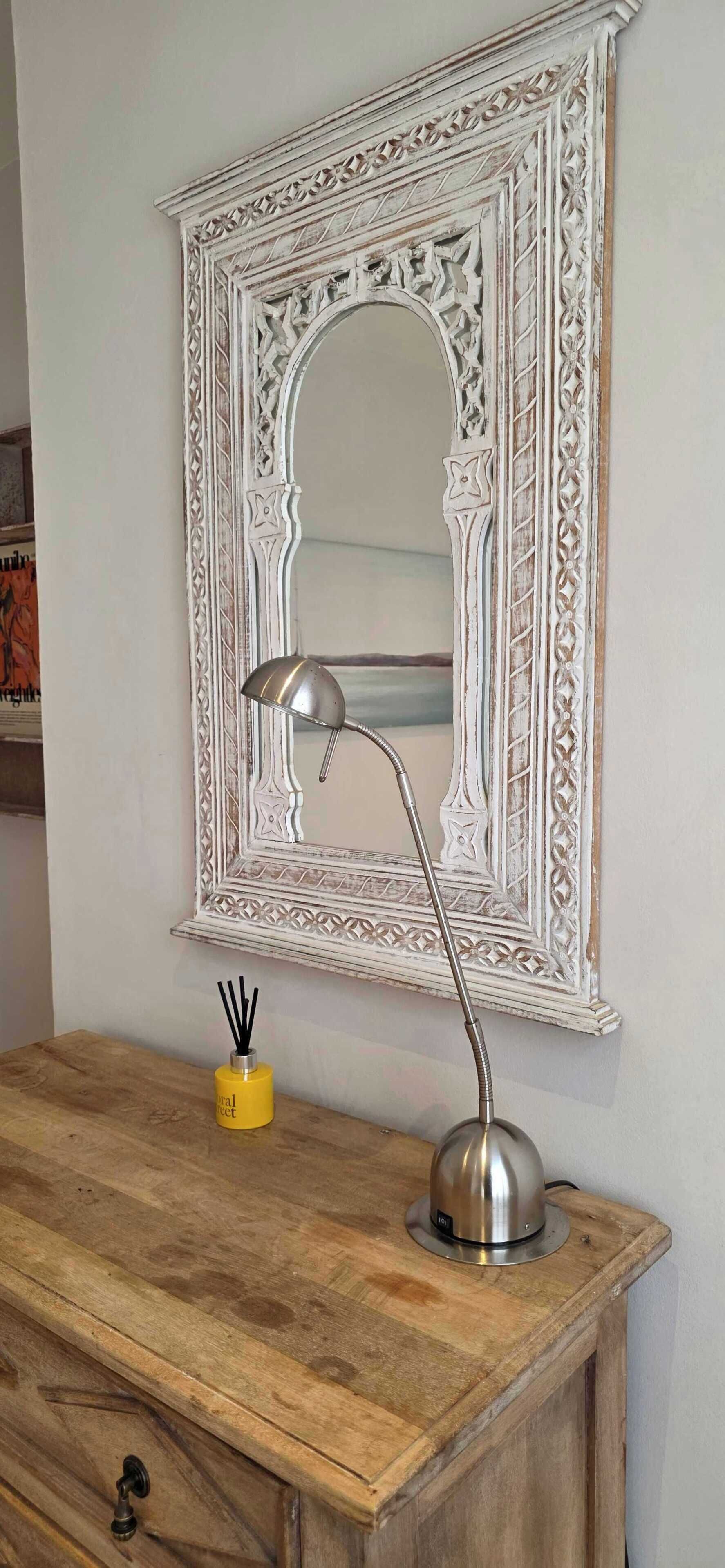 A mirror with ornate white frame, a desk with a lamp, and a yellow candle holder.