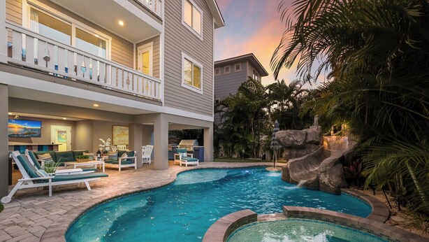 A two-story building with a pool area featuring lounge chairs, a barbecue, and a waterfall. - Beach & Bay by Beach Boutique Rentals (Bradenton Beach)