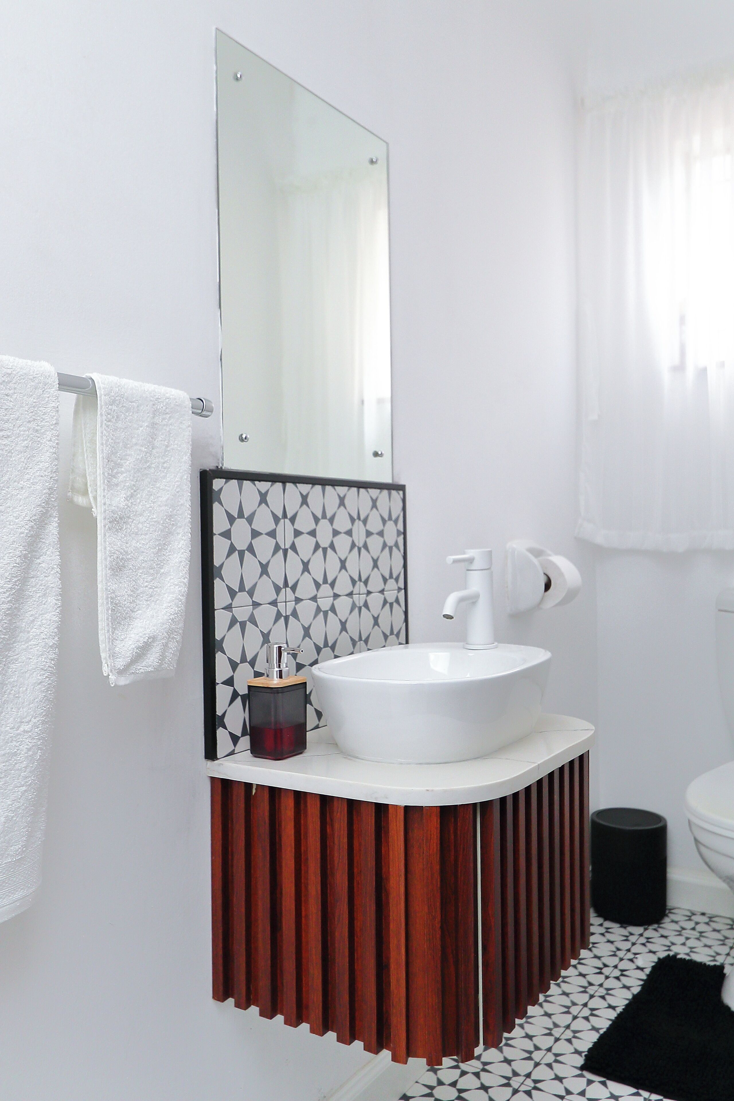 Ein Badezimmer mit einem weißen Waschbecken, einem Spiegel und einer Wand mit Muster.