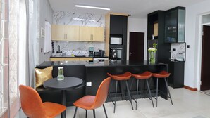 A modern kitchen with marble backsplash, wooden cabinets, and a central island with bar stools. - Motswana Suite: Calm & Cozy 2-bedroom stylish apartment (Gaborone)