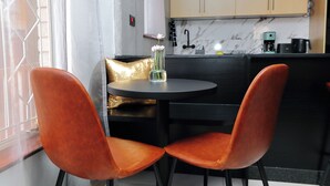 A modern kitchen with a marble backsplash, a round table, and two orange chairs. - Motswana Suite: Calm & Cozy 2-bedroom stylish apartment (Gaborone)