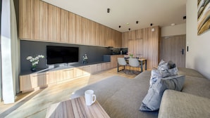 A modern living space with a flat-screen TV, wooden cabinetry, a dining area, and a sofa. - Apartamenty Sun & Snow Greeneri Park (Świnoujście)