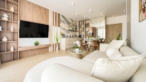 A modern living room with a large flat-screen TV, a sofa, and a dining area with a table and chairs. - Apartamenty Sun & Snow Greeneri Park (Świnoujście)