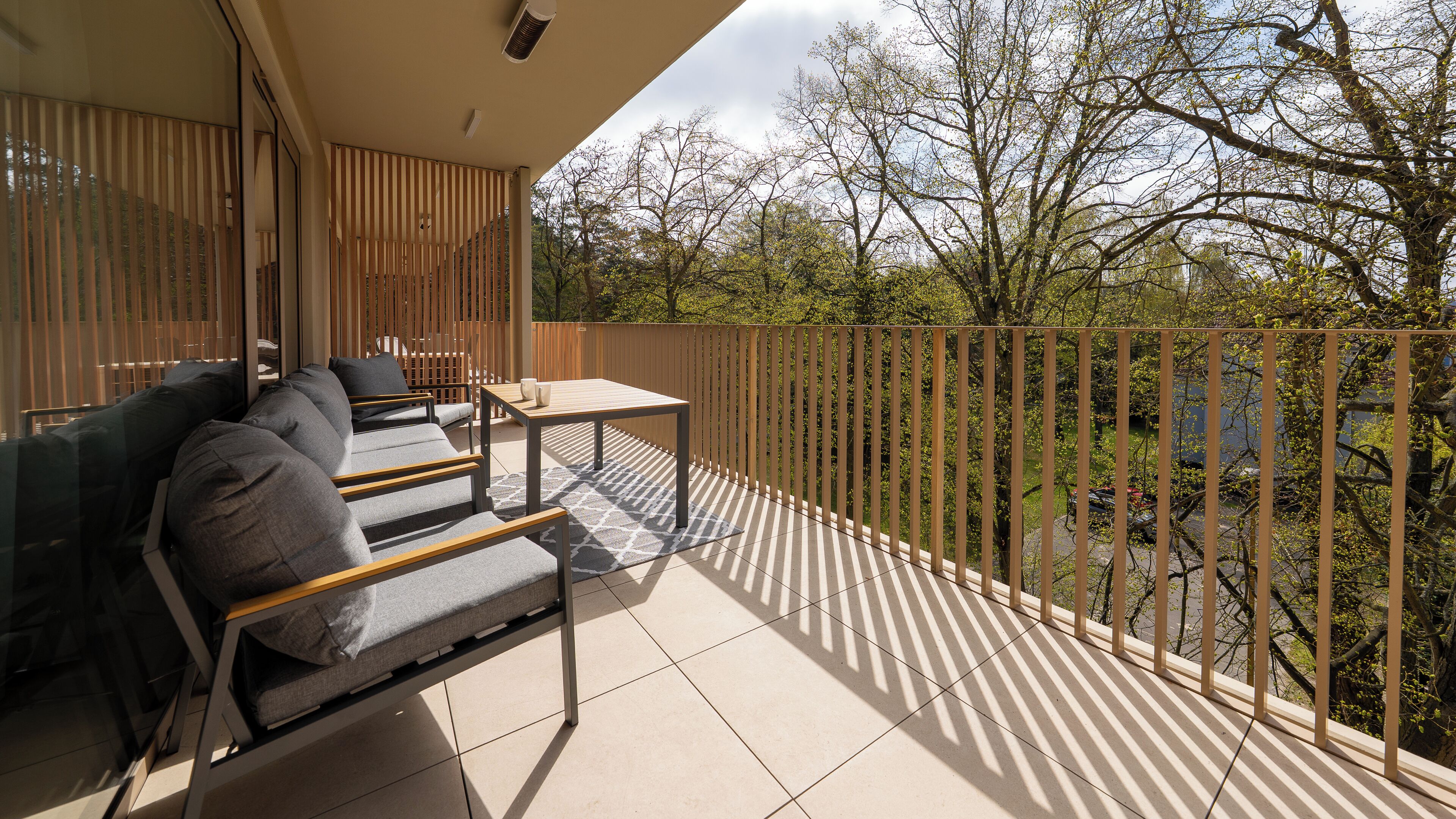 A balcony with a sofa, a table, and a view of trees and a fence.