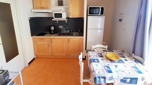 Ett kompakt kök med mikrovågsugn, kaffebryggare och ett litet kylskåp. Här finns ett matbord med stolar och ett fönster med gardiner.