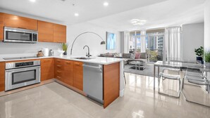 Una cocina moderna con electrodomésticos integrados, un comedor con mesa de vidrio y vistas a la ciudad.