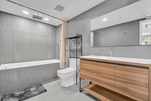 Un baño moderno con bañera, inodoro, tocador y un espejo grande.