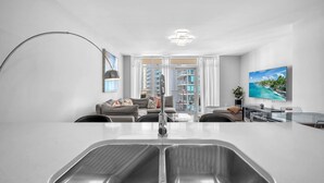 Una cocina moderna con una isla grande, un comedor con mesa de vidrio y una sala de estar con sofá y televisión.