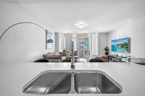 A modern kitchen with a large island, a dining area with a glass table, and a living room with a sofa and a TV. - Spacious 2BR Miami | Pool & Gym | near Midtown (Miami)