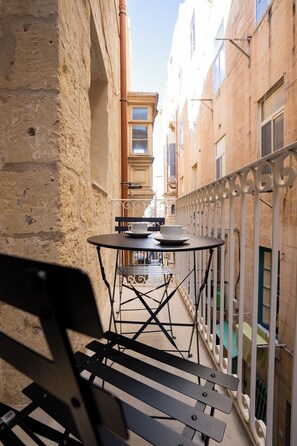 Un étroit couloir extérieur avec une table et des chaises en métal, un banc et une rambarde blanche.