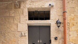 Un bâtiment en pierre avec une porte à deux battants de couleur grise, une petite fenêtre au-dessus de la porte et un tuyau métallique sur le côté droit.