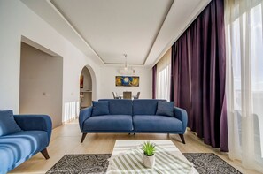 Un salon moderne avec un canapé bleu, une table à manger avec des chaises et une plante en pot posée sur un tapis à rayures.