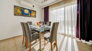 A dining area with a glass table, four grey upholstered chairs, a chandelier, and a large abstract painting on the wall. - Incredible Sliema Harbour Penthouse With Jacuzzi (Sliema)