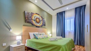 A hotel room with a wooden headboard, a green bedspread, a nightstand with a lamp, and a large painting above the bed. - Incredible Sliema Harbour Penthouse With Jacuzzi (Sliema)
