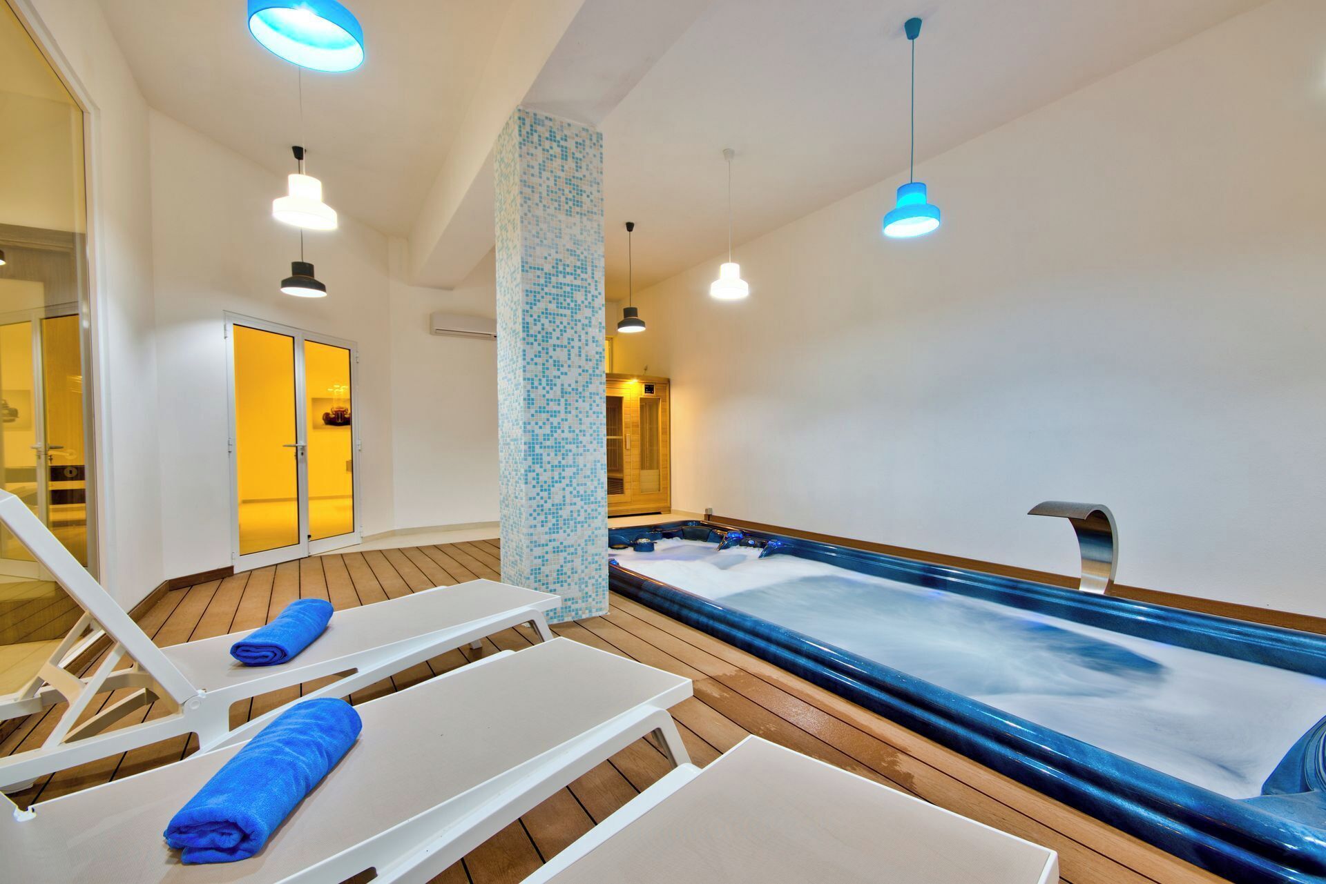 A spa area with a hot tub, wooden flooring, white lounge chairs, and blue towels.