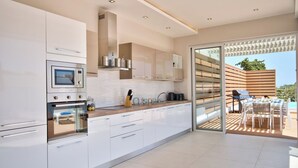 A modern kitchen with white cabinets, a built-in oven, and a large window overlooking a patio with outdoor seating. - Extraordinary Villa With Private Pool & Steamsauna (Mellieha)