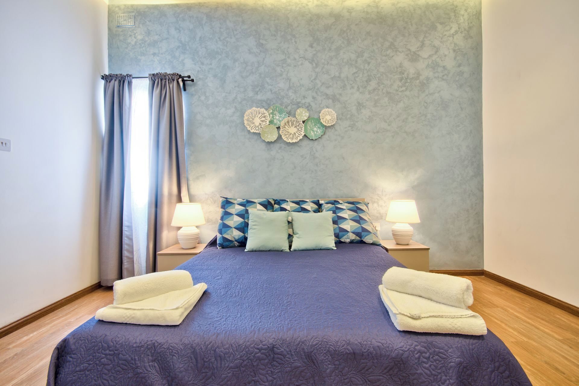 Une chambre à coucher avec un lit, deux lampes de chevet, un mur décoré de fleurs en papier et une fenêtre avec des rideaux.