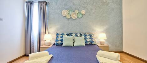 Une chambre à coucher avec un lit, deux lampes de chevet, un mur décoré de fleurs en papier et une fenêtre avec des rideaux.