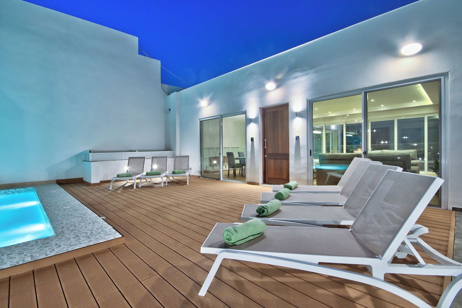 A modern outdoor pool area with lounge chairs and a glass-enclosed dining area.