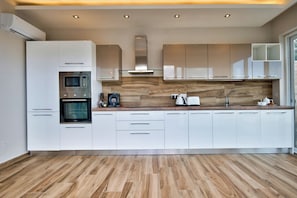 Una cocina moderna con armarios blancos, horno empotrado, microondas y cafetera.