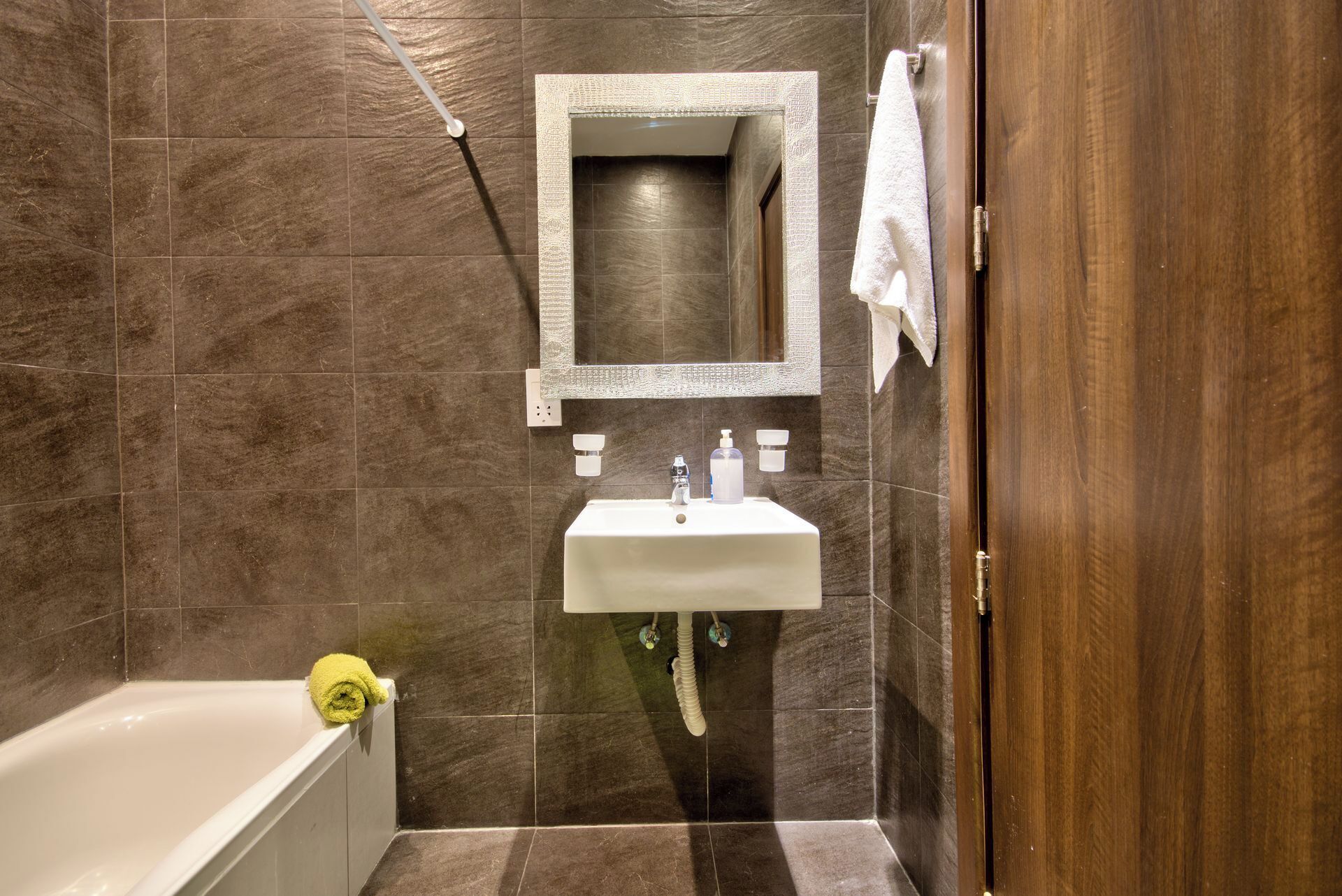 Un baño con lavamanos blanco, espejo y perchero.