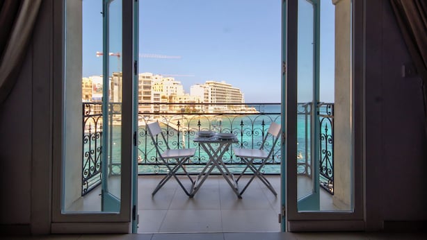 Un balcón abierto con una mesa y sillas, con vistas a la ciudad y al mar.