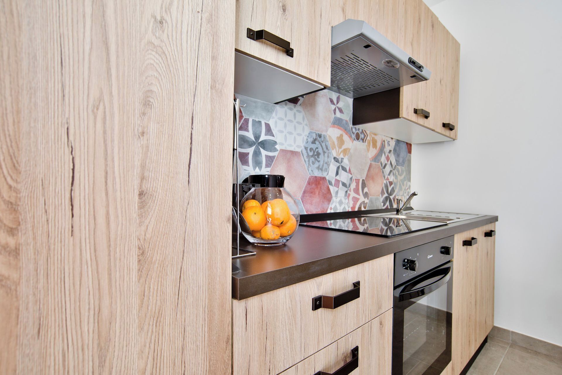 A modern kitchen with wooden cabinetry, a tiled backsplash, a stainless steel sink, and a built-in oven.