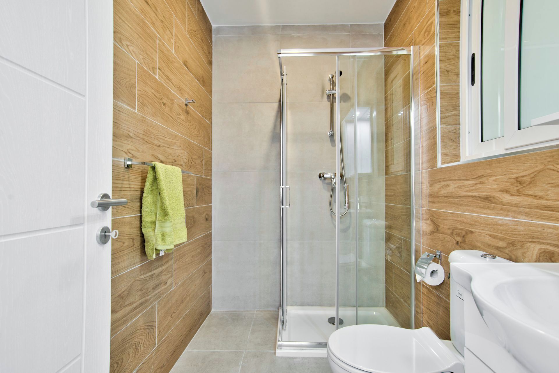 A modern bathroom with a glass shower enclosure, a white toilet, and wooden wall panels.