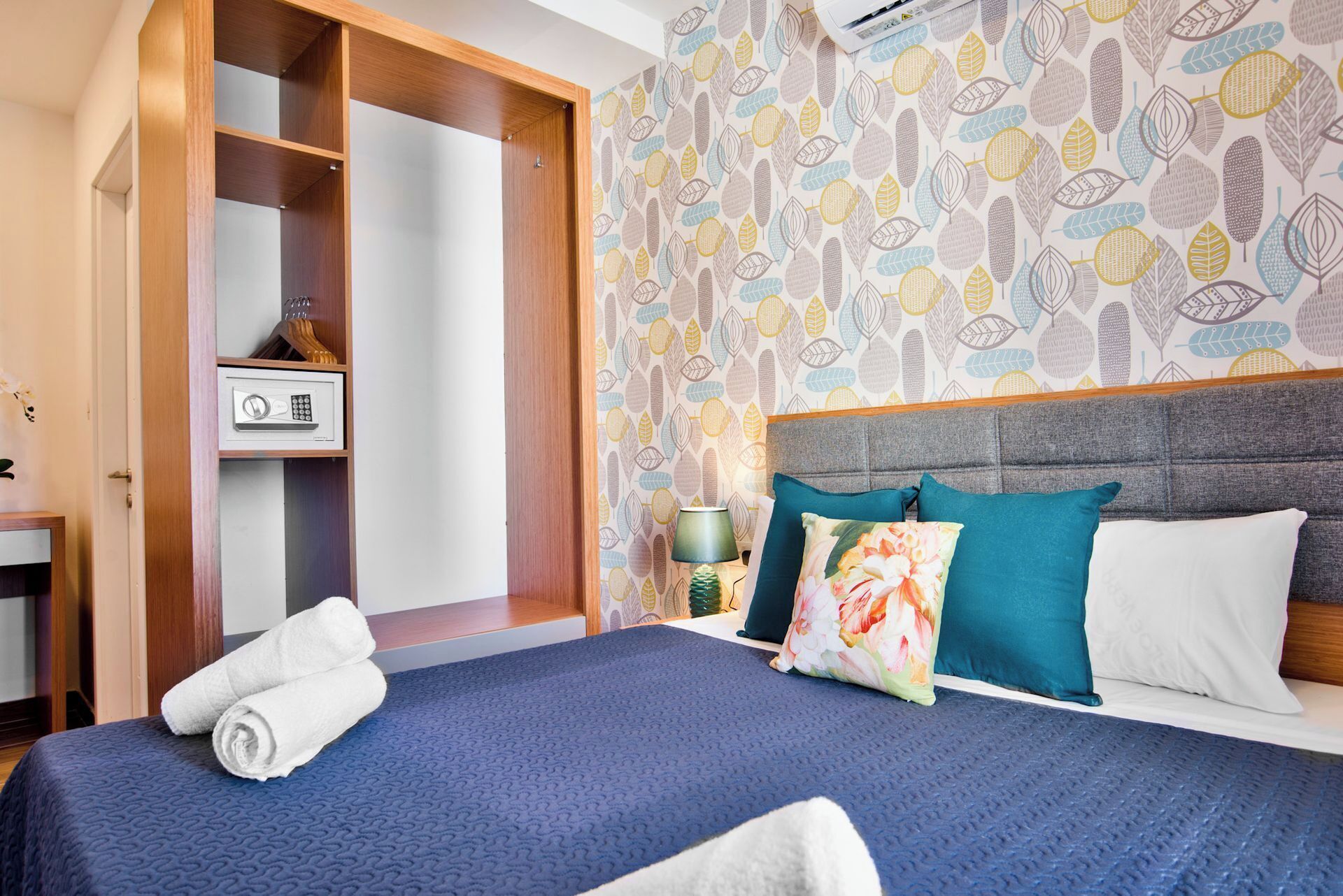 Ett hotellrum med en säng, en garderob, ett skrivbord och en tapet med mönster.