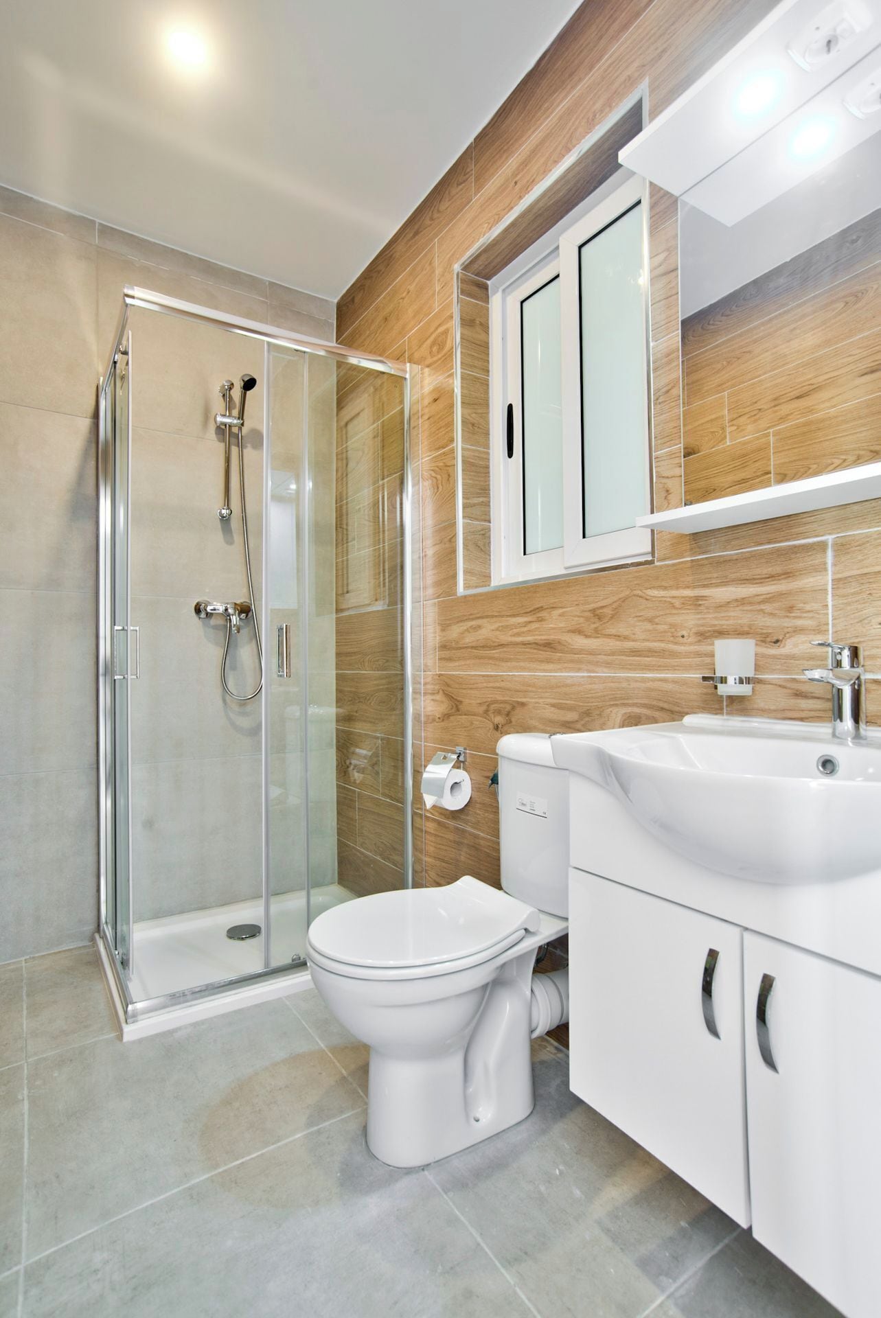 A modern bathroom with a glass shower enclosure, a toilet, and a sink with a wooden wall backdrop.