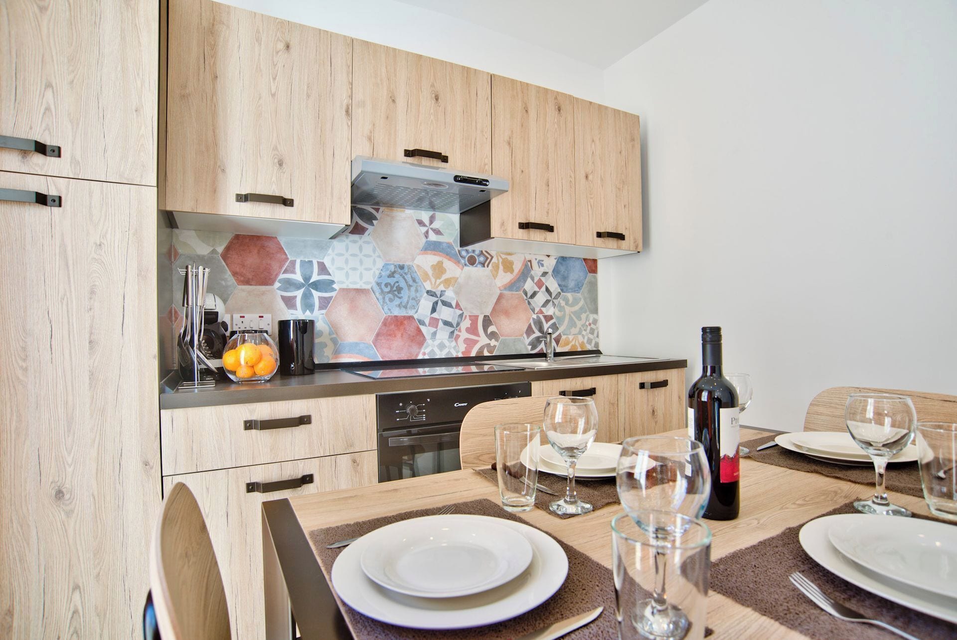 Eine moderne Küche mit Holzschränken, einer farbenfrohen Spritzschutzleiste und einem Essbereich, der für eine Mahlzeit gedeckt ist.