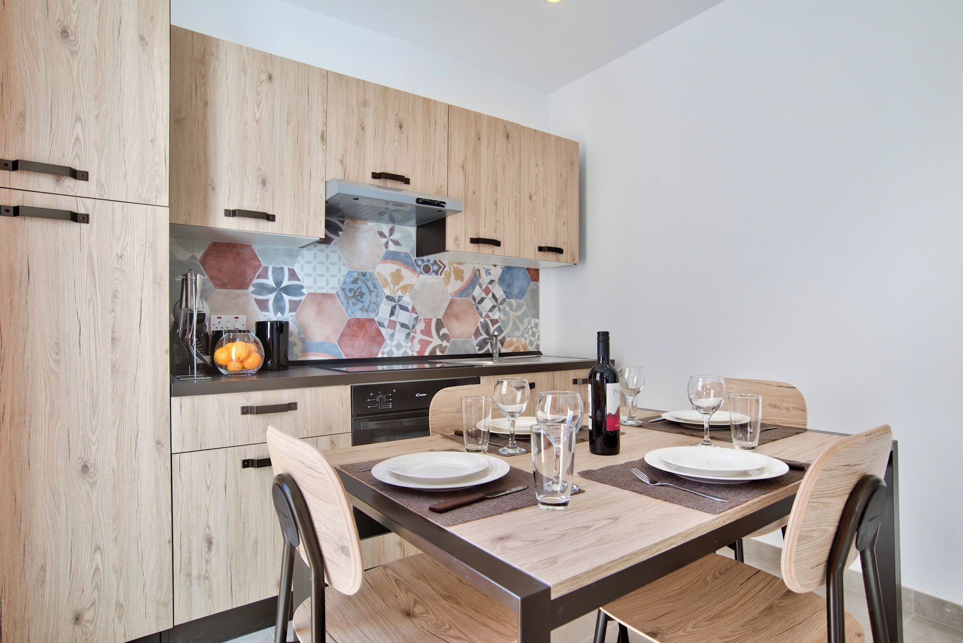 A modern kitchen with wooden cabinets, a tiled backsplash, and a dining area with a wooden table set for four.