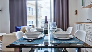 A dining table set with white bowls, wine glasses, and a bottle of wine, with a view of a balcony and building in the background. - Central Sunny Apartment + Views of Valletta City (Sliema)