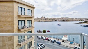 A building with balconies overlooking a marina with boats and a cityscape in the background. - Central Sunny Apartment + Views of Valletta City (Sliema)