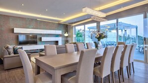 Un espace repas moderne avec une grande table et des chaises, un téléviseur et une vue sur l’extérieur.