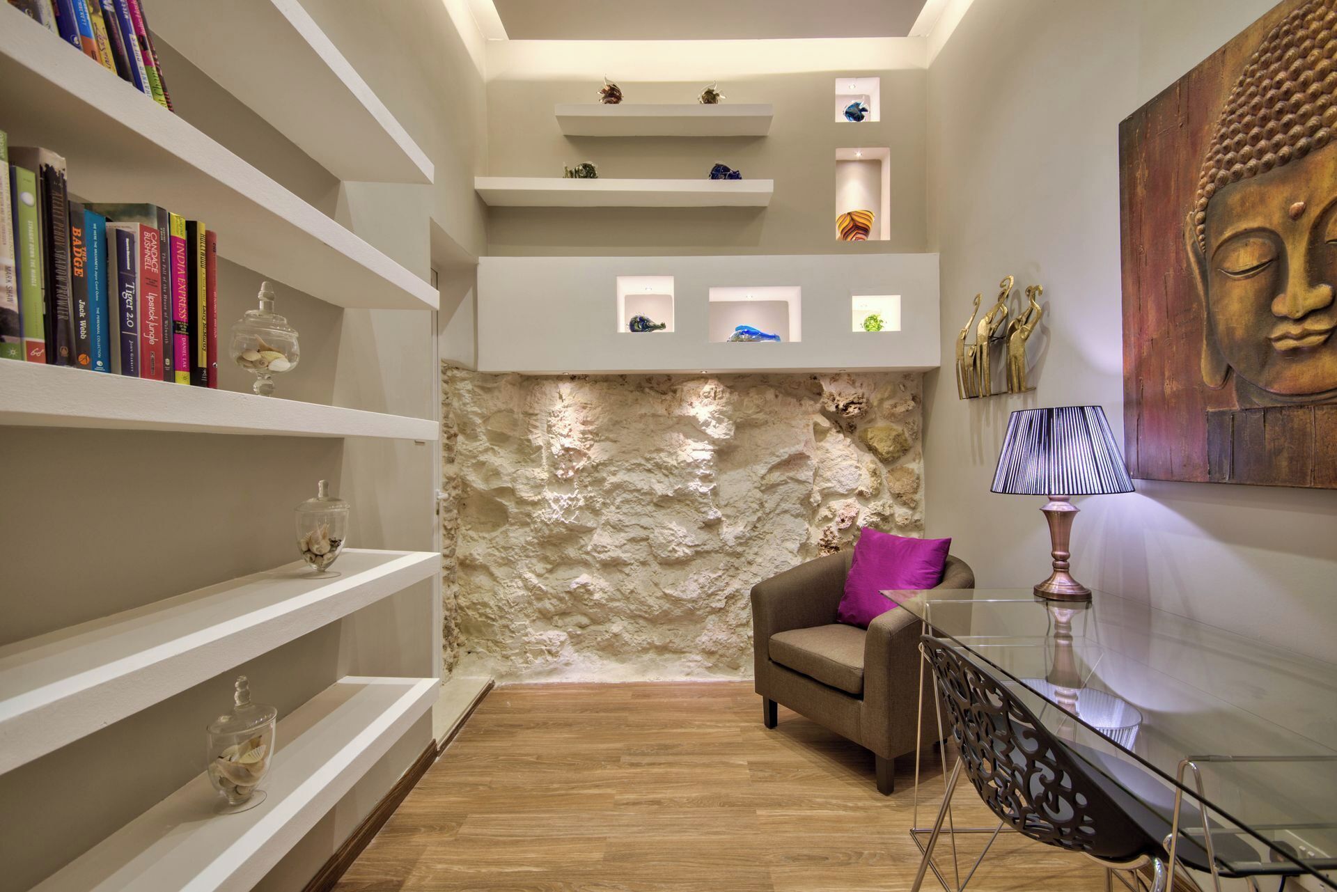A modern living room with a stone accent wall, a Buddha painting, and a glass table with a lamp.